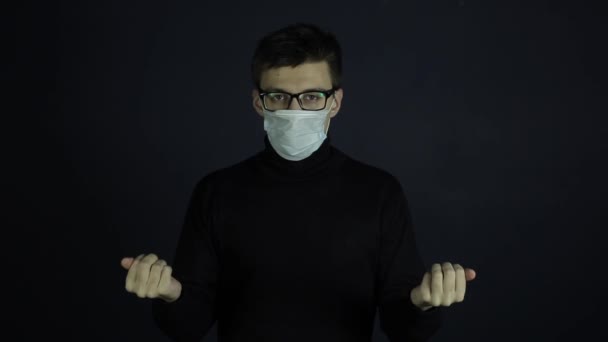 A caucasian man wearing a medical mask holding coronavirus COVID-19 models in his hands. Shaking his head. Black dark background, clothes. — Stock Video