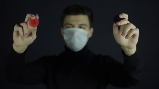 Uno scienziato caucasico che indossa una maschera protettiva guardando e indicando la fotocamera due modelli COVID-19 coronavirus. Sfondo scuro. Isolato. Mani . — Video Stock