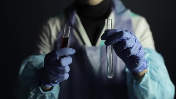 Um close-up em um cientista com óculos misturando soluções em lâmpadas. Fundo escuro, uniforme médico, macacão . — Vídeo de Stock