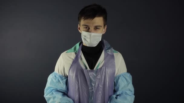 Un jeune médecin caucasien clignote la lumière à la caméra. Abandonner les pouces. Fond noir foncé. Porter des vêtements médicaux . — Video
