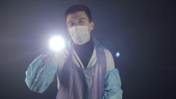 A young caucasian doctor flashing the light at the camera. Studying a COVID-19 coronavirus model. Black dark background. Wearing medical clothes. — Stock Video