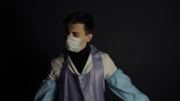 Un jeune homme caucasien portant une combinaison de protection médicale et un masque respiratoire. Isolé sur fond noir. Fatigué, dansant. Coronavirus . — Video