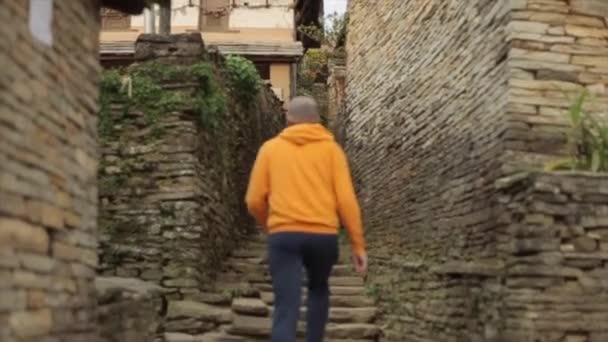 Un hombre caucásico caminando por la estrecha calle de piedra nepalesa. Nepal, Katmandú, pueblo de montaña . — Vídeo de stock