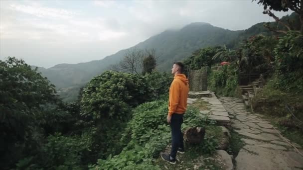 नेपाल में एक पहाड़ी के कगार पर खड़ा एक कोकेशियान पर्यटक। पर्वत परिदृश्य . — स्टॉक वीडियो