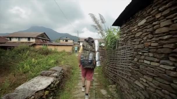 Kaukasische toeristen, wandelaars met rugzakken trekking door Nepal, nepalese dorp. Achteraanzicht. — Stockvideo