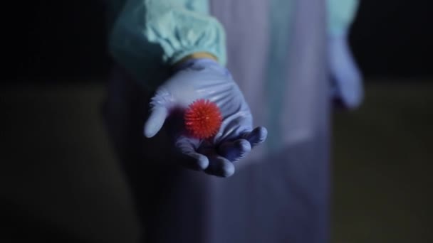 Close up de um cientista em roupas médicas de proteção, terno apontando para a câmera um modelo de coronavírus COVID-19. Fundo escuro . — Vídeo de Stock