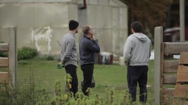 Bobruisk, Bielorrússia - 14 de outubro de 2019: Três homens estão discutindo ativamente algo no quintal da fazenda com edifícios — Vídeo de Stock