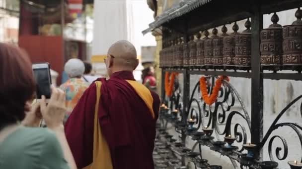 Kathmandu, Nepal - 19 november 2019: Een nepalese monnik in traditionele kledij passeert gebedswielen. Een toerist filmt hem. Kathmandu, Azië, Nepal. — Stockvideo