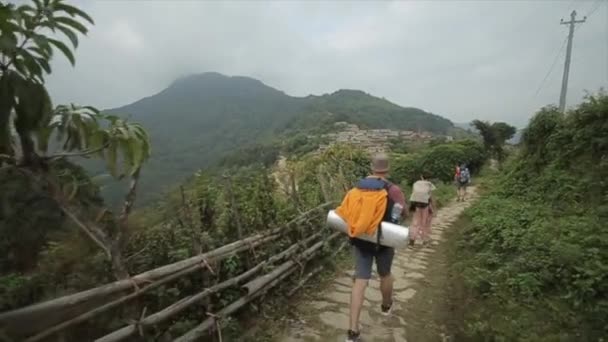Kaukasische toeristen, wandelaars met rugzakken trekking in Nepal, nepalese dorp. Achteraanzicht. Vrouwen, mannen. — Stockvideo