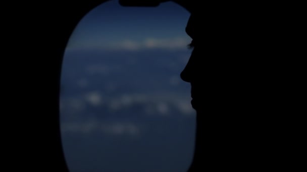 Uma pessoa silhueta olhando para fora da janela de aviões no céu, nuvens. Vista próxima. Cara características . — Vídeo de Stock