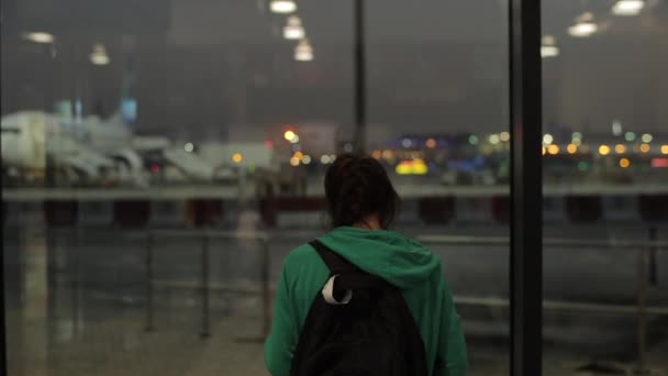 Ein junges Mädchen, eine wartende Frau, die nachts auf einem Flughafen Flugzeuge fotografiert. Rückansicht. — Stockvideo