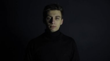 Beyaz bir genç adam tıbbi koruyucu maske takıyor. Siyah arka plan, kıyafetler. Coronavirus koruması.
