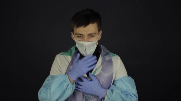 Ein junger kaukasischer Mann hustet und setzt sich eine medizinische Maske auf. Vereinzelter schwarzer Hintergrund. Coronavirus Covid19 — Stockvideo