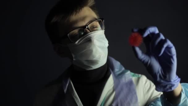 Uno scienziato in abiti protettivi guardando un modello COVID-19 coronavirus. Sfondo scuro . — Video Stock