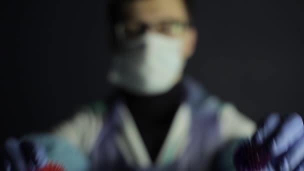 Un científico con ropa protectora señalando a la cámara dos modelos de coronavirus COVID-19. Fondo oscuro . — Vídeos de Stock