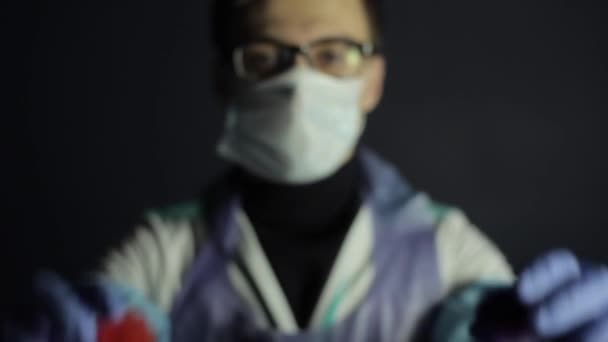 Een wetenschapper in beschermende kleding wijst naar de camera twee Coronavirus Covid-19 modellen. Donkere achtergrond. — Stockvideo
