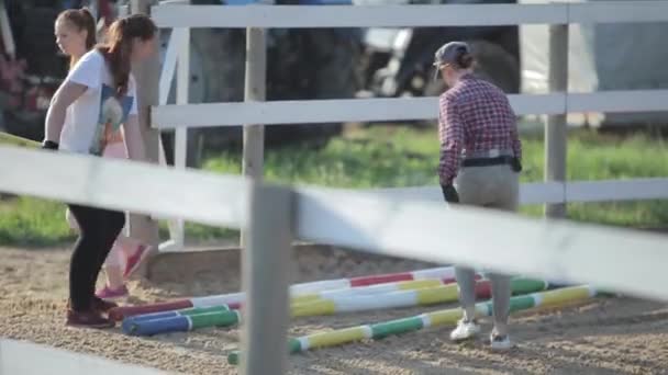 Mińsk, Białoruś - 19 lipca 2019: młode dziewczęta pomagają nieść sprzęt jeździecki na farmie koni. Z przodu. Zbliżenie — Wideo stockowe