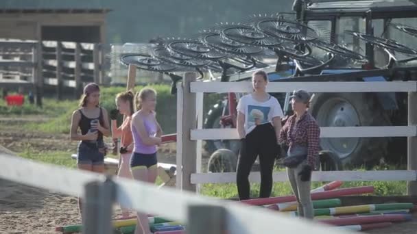 Minsk, Belarus - 19 Temmuz 2019: Genç kızlar at çiftliğindeki ahıra atlama ekipmanları taşıyorlar. Arka plan — Stok video