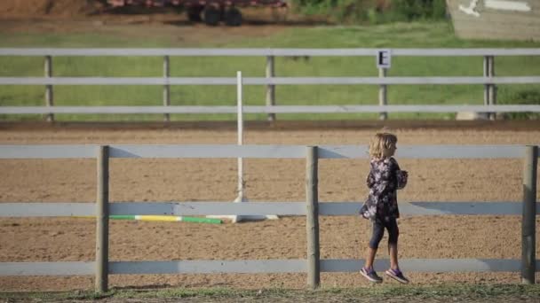 Минск, Беларусь - 19 июля 2019 года: Маленькая девочка прыгает с деревянного забора конного загона на конной ферме. Вид сзади — стоковое видео