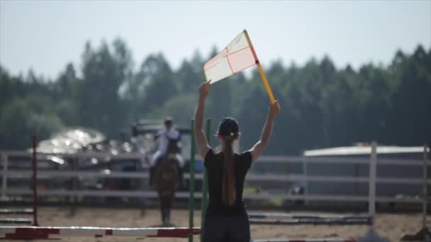 Minsk, Bielorrússia - 19 de julho de 2019: Uma menina segura uma bandeira acima da cabeça para sinalizar o início das competições equestres. Visão traseira — Vídeo de Stock