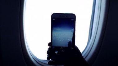 Gökyüzü ve bulutların cep telefonuyla uçağın camından fotoğraf çeken birinin yakın görüntüsü..