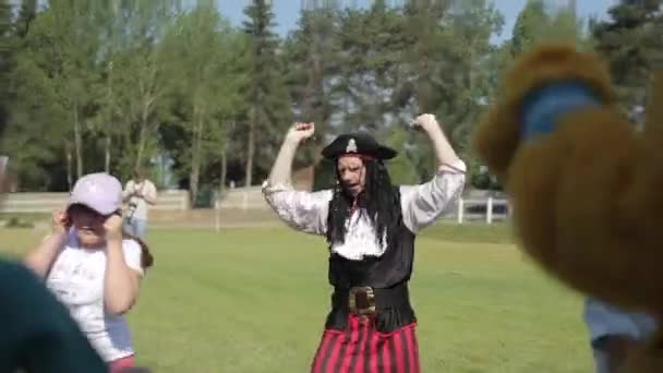 Минск, Беларусь - 19 июля 2019 года: Актер в пиратском костюме танцует с детьми на лужайке на лошадином ранчо. Крупный план — стоковое видео