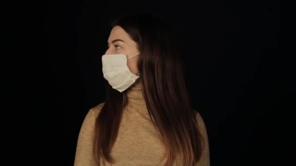 女の子は周りを見回して保護マスクを外してサ・カメラを見て。コロナウイルスだ。GOVD-19 。隔離された黒の背景. — ストック動画