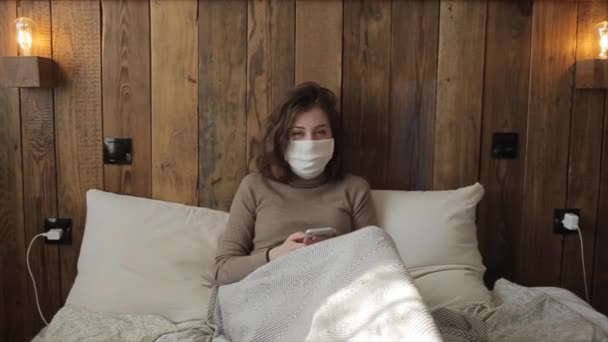 Mooi jong meisje met een beschermend masker communiceert via de telefoon tijdens quarantaine. Coronavirus. COVID-19 — Stockvideo