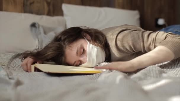 A young attractive girl in a protective mask slams on the bed and calls her dog. Coronavirus. COVID-19 — Stock Video