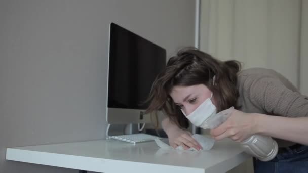 Mladá dívka v karanténní ochranné masce pečlivě dezinfikuje stůl doma. — Stock video