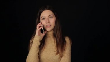 Sarı elbiseli şirin bir kızın portresi cep telefonuyla konuşuyor ve siyah arka planda yalnız başına gülüyor.