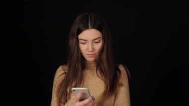 Sarı elbiseli tatmin olmuş bir kadın kameraya bakarken siyah arka planda neşeli bir cep telefonu kullanıyor.