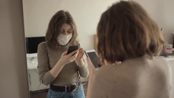 Skyddsmaskerad ung flicka pratar i telefon framför spegeln.Coronavirus.COVID-19 — Stockvideo