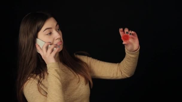 Bájos kaukázusi lány néz egy koronavírus COVID-19 piros modell és beszél telefonon. Sötét háttér. Elszigetelt — Stock videók