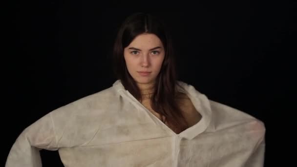 Кавказька дівчина одягає захисний костюм і дивиться на камеру. Проти коронавірусу COVID-19 — стокове відео