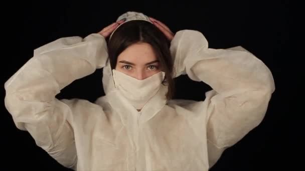 Дівчина знімає свій захисний костюм і медичну маску і розсовує волосся. Дівчина стає дуже красивою і дивиться на камеру. коронавірус COVID-19 — стокове відео