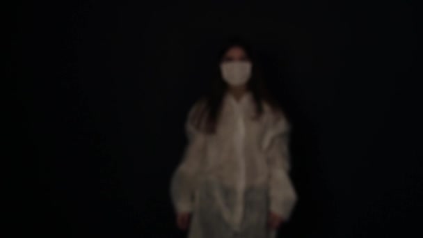 Молода мила біла дівчина з'являється з темряви і ставить медичну маску. коронавірус COVID-19 — стокове відео