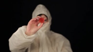 Koruyucu takım elbiseli beyaz bir kadın doktor kamera Coronavirus COVID-19 modellerine bakıyor ve işaret ediyor. Karanlık arka plan. İzole edilmiş. Eller yukarı. Kadın bilim adamı.