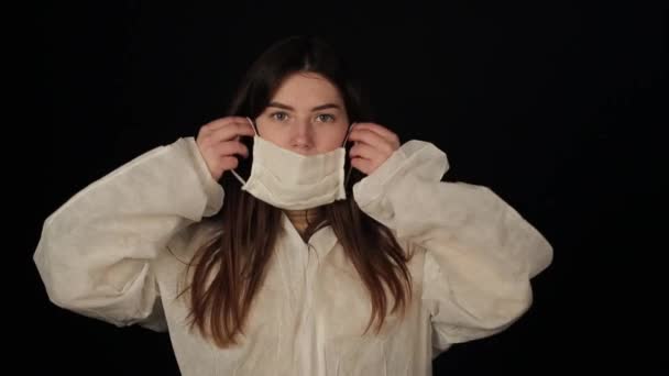 Genç kadın bilim adamı koruyucu giysiler, takım elbise, maske ve eldiven giyiyor. İzole edilmiş siyah arka plan. Coronavirus, COVID19. Kız tıbbi maske takıyor. — Stok video