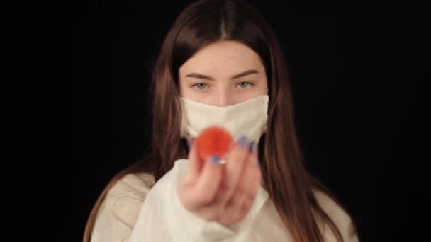 Gros plan de la fille caucasienne en vêtements de protection et masque médical regardant un modèle COVID-19 coronavirus. Fond sombre . — Video