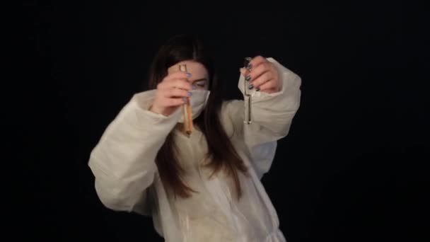 보호용 양복을 입고 의료용 마스크를 쓴 미치광이 소녀가 액체와 춤을 추는 카메라 실험실 플라스크를 보여 주고 있다 — 비디오