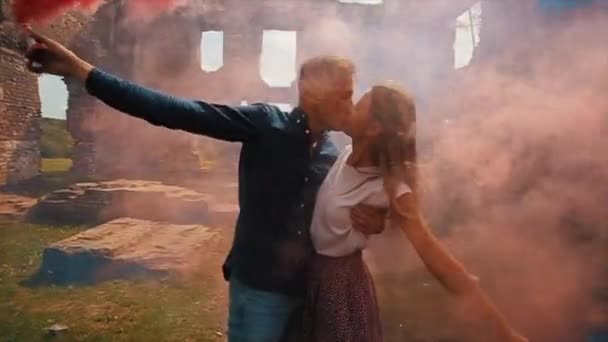 Vista de perto de um jovem lindo casal beijando segurando bombas de fumaça em suas mãos — Vídeo de Stock