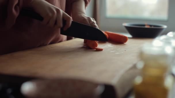 Primer plano de las manos de una joven mujer picando zanahorias con un cuchillo grande para cocinar en su cocina — Vídeos de Stock