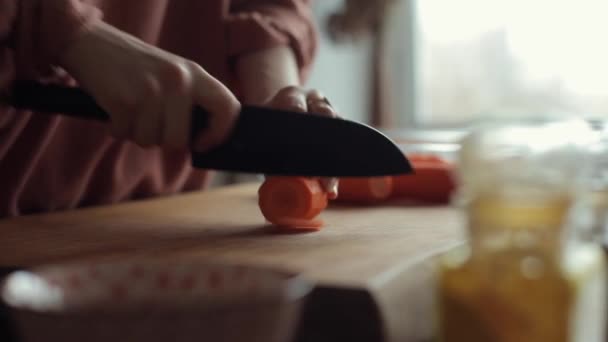 La niña corta zanahorias en círculos con un cuchillo grande en la encimera de su cocina. Primer plano — Vídeo de stock