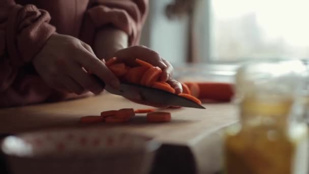 Primer plano de las manos de una joven que apila zanahorias picadas en un tazón grande en la mesa de la cocina — Vídeos de Stock