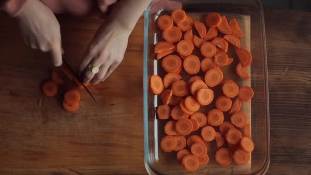 Close-up das mãos de uma jovem menina cortando cenouras e dobrá-lo em uma tigela de vidro grande em sua cozinha. Vista de cima — Vídeo de Stock