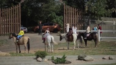 Minsk, Belarus - 19 Temmuz 2019: At sırtında kızlar ve bir grup insan çiftliğin açık kapısının yanında duruyor. Arka plan