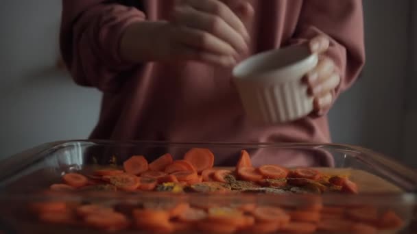 Hände einer jungen Frau streuen in ihrer Küche ein Gericht mit gehackten Möhren. Nahaufnahme — Stockvideo