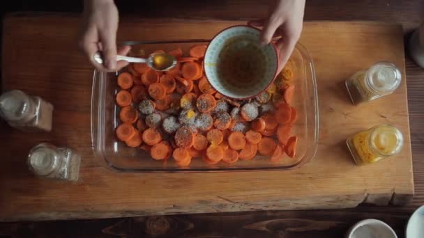 Ein junges Mädchen gießt Sauce auf gehackte Möhren mit Gewürzen in eine große Glasschüssel. Blick von oben. Nahaufnahme — Stockvideo