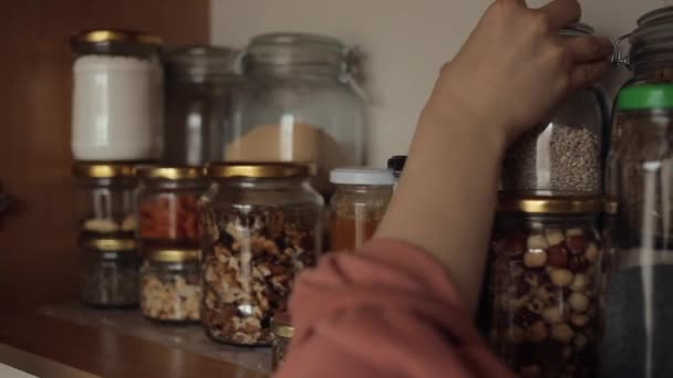 La jeune fille organise des boîtes de conserve avec des gruaux et des épices pour cuisiner sur une étagère dans le placard de la cuisine. Gros plan — Video